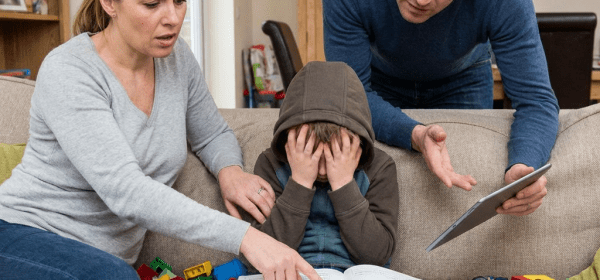 Stressed parents and child struggling with homework and a tablet on a couch.