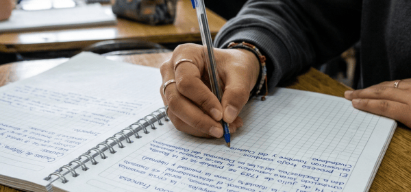 Student writing handwritten notes in a spiral notebook during class